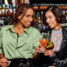 Two Black women enjoying cocktails together at a bar after work